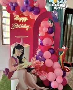 a woman sitting in front of a birthday arch with balloons and flowers on top of it