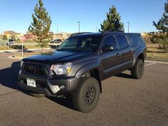 a black toyota truck parked in a parking lot next to some trees and bushes on a sunny day