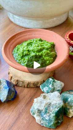 a bowl filled with green sauce sitting on top of a wooden table next to rocks