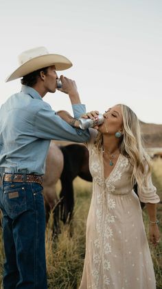 a man standing next to a woman wearing a cowboy hat and drinking from a bottle