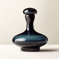 a black and blue glass vase sitting on top of a table next to a white wall