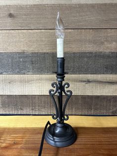 a small black candle holder on a wooden table next to a wood planked wall