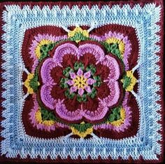 a crocheted square with a flower in the center on a black table top