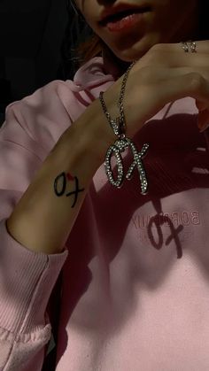 a woman wearing a pink hoodie holding onto her wrist with the word xo tattooed on it