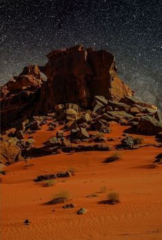 the night sky is filled with stars above some rocks and sand in an arid area