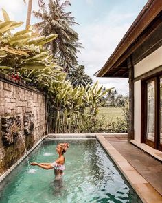 a woman standing in the middle of a pool next to a stone wall and palm trees