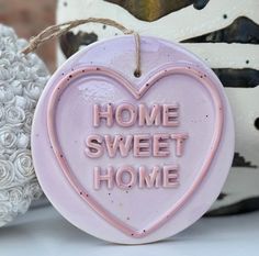 a pink heart shaped sign that says home sweet home on it next to some white flowers