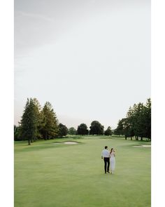 a man and woman walking across a lush green field next to a golf ball hole