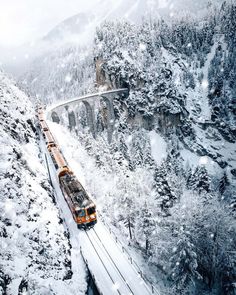 a train traveling over a bridge in the middle of snow covered mountains with trees on both sides