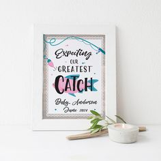 a white framed print with the words expecting our greatest catch on it next to a candle