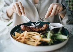 a woman is eating steak and french fries with a fork in her hand while sitting at a table