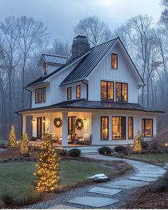 a white house with christmas lights on the front porch and trees in the back yard