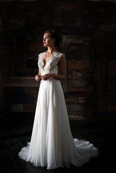 a woman standing in front of a wooden wall wearing a white dress with ruffles