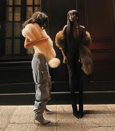 two mannequins are standing in front of a building and one is holding a fur coat