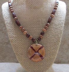 What an eye-catching wood pendant necklace! This one-of-a-kind design will wow you.  The light-colored wood is lamented and splashed with a wine-colored design. The necklace is accented with wine-colored seed beads and palmwood beads. *Necklace length: 21 inches *Pendant size: 1.5 inches in diameter   *Accent beads: Seed and wood *Dark-brown cotton cord *Antique brass pinch bail *Antique brass clasp Gift Brown Wooden Beaded Necklaces, Brown Wooden Beaded Necklace Gift, Wooden Brown Beaded Necklace Gift, Mahogany Wooden Beads Jewelry, Mahogany Colored Wooden Bead Jewelry, Necklace With Beads, Light Colored Wood, Wood Jewelry, Wood Pendant