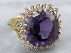 The halo style is pretty and bold, both framing and protecting the stone with the protective prong setting surrounding the diamonds and multiple prongs encasing the stone. This is one of our finest amethyst, a natural stone, deep purple, with fine, bright blue highlights. Outstanding in quality and construction, wearable and versatile. Metal: 18K Yellow Gold Gem: Amethyst Gem Measurements: 13.7 x 13.1 mm, Square Cushion Cut Accents: 22 Diamonds totaling .75 Carats, F in Color, VS in Clarity Ring Luxury Amethyst Ring With Halo Setting, Luxury Purple Diamond Ring With Halo Setting, Luxury Amethyst Ring With Diamond Halo Setting, Bright Blue Highlights, Yellow Gold Sapphire Ring, Gold Amethyst Ring, Blue Highlights, Diamond Cocktail Ring, Halo Style