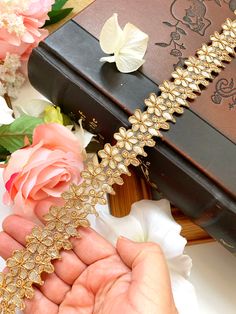 a hand is holding a gold bracelet with flowers on it and a book in the background