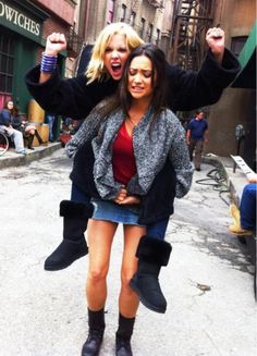 two women standing on the street with their arms in the air and one holding up her leg