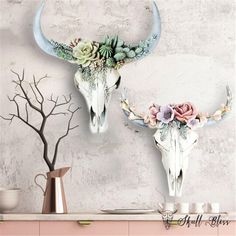 two deer skulls decorated with flowers and succulents on a wall above a shelf