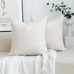 two white pillows sitting on top of a couch next to a vase filled with flowers