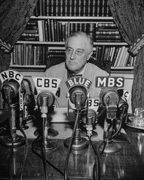 an old black and white photo of a man sitting at a table surrounded by microphones