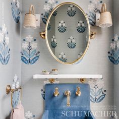 a bathroom with blue and white wallpaper, gold faucets and a round mirror