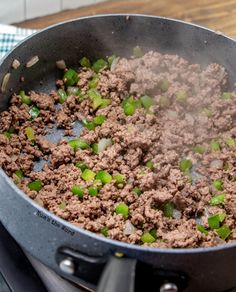 a pan filled with meat and green onions cooking on top of a stove burner