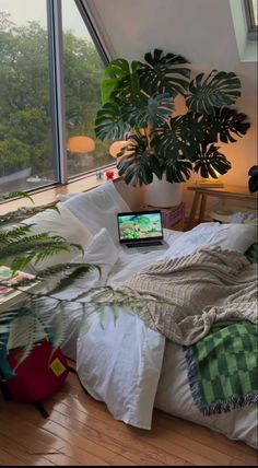 a laptop computer sitting on top of a bed next to a plant in a room