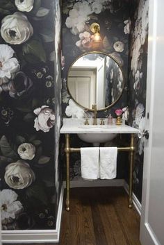 a small bathroom with floral wallpaper and gold sink faucet, white toilet paper