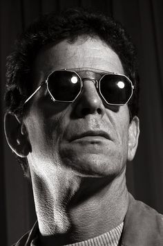 a man with sunglasses on his face looking off to the side in front of a curtain