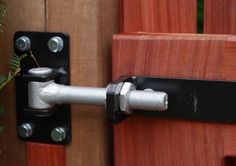 a close up of a door handle on a wooden fence with green plants in the background