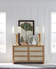 a dresser with two lamps on top of it next to a painting and framed pictures