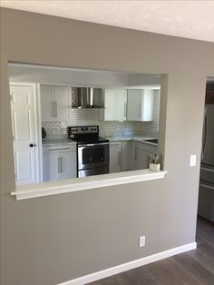 an empty kitchen with stainless steel appliances and white cabinets is seen through the mirror on the wall