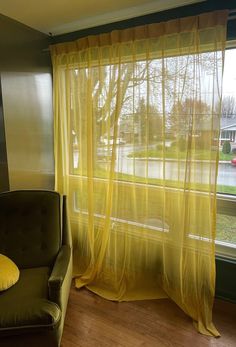 a chair sitting in front of a window with yellow drapes on the windowsill