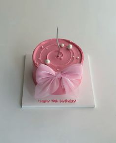 a pink birthday cake decorated with pearls and a bow