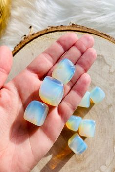 a hand is holding some blue and yellow ice cubes in front of a wood slice