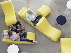 three people are sitting on yellow couches in an office setting with tables and chairs