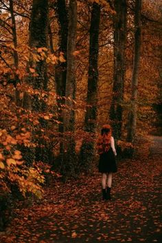 a woman with red hair walking down a leaf covered path in an autumnal forest