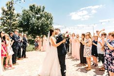 a bride and groom kissing in front of their wedding party at the end of an outdoor ceremony