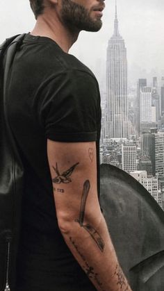 a man with a tattoo on his arm standing in front of a cityscape