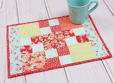 a coffee cup sitting on top of a table next to a red and green patchwork place mat