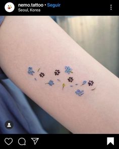 a tattoo with blue flowers and paw prints on the arm