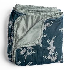 a blanket with white flowers on it is folded up in front of a white background