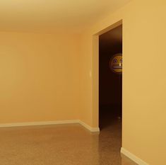 an empty room with yellow walls and a door leading to another room that has a clock on the wall