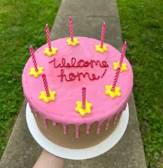 a birthday cake with candles and welcome home written on the top is being held by someone