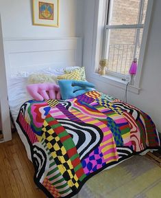 a bed with a colorful blanket and pillows on top of it next to a window