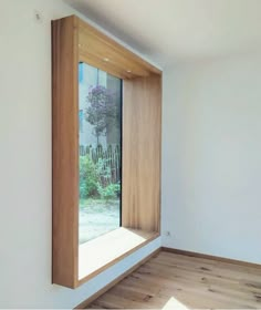 an empty room with wooden floors and a window that looks out onto the garden outside