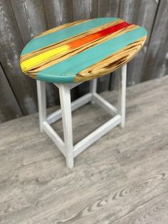 a colorful wooden stool sitting on top of a hard wood floor next to a wall