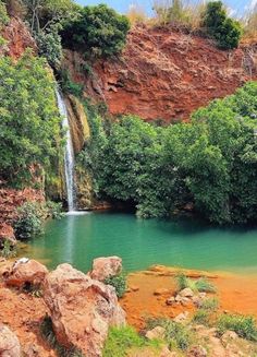 there is a small waterfall in the middle of this lake with green trees around it