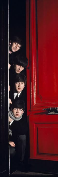 a group of young men standing next to each other in front of a red door